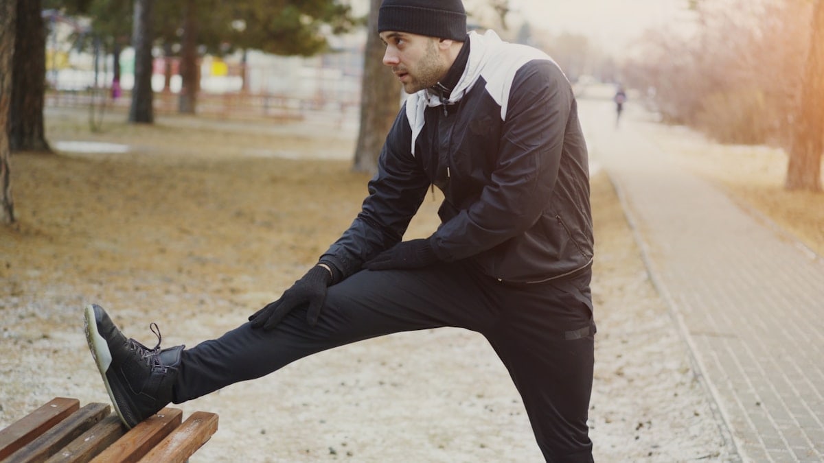Young man runner doing stretching exercise preparing for morning workout and jogging in winter park